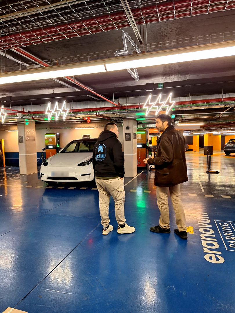 Jorge Cristóbal Román con su Tesla Model Y blanco, taxi eléctrico, en un parking con puntos de recarga en Madrid